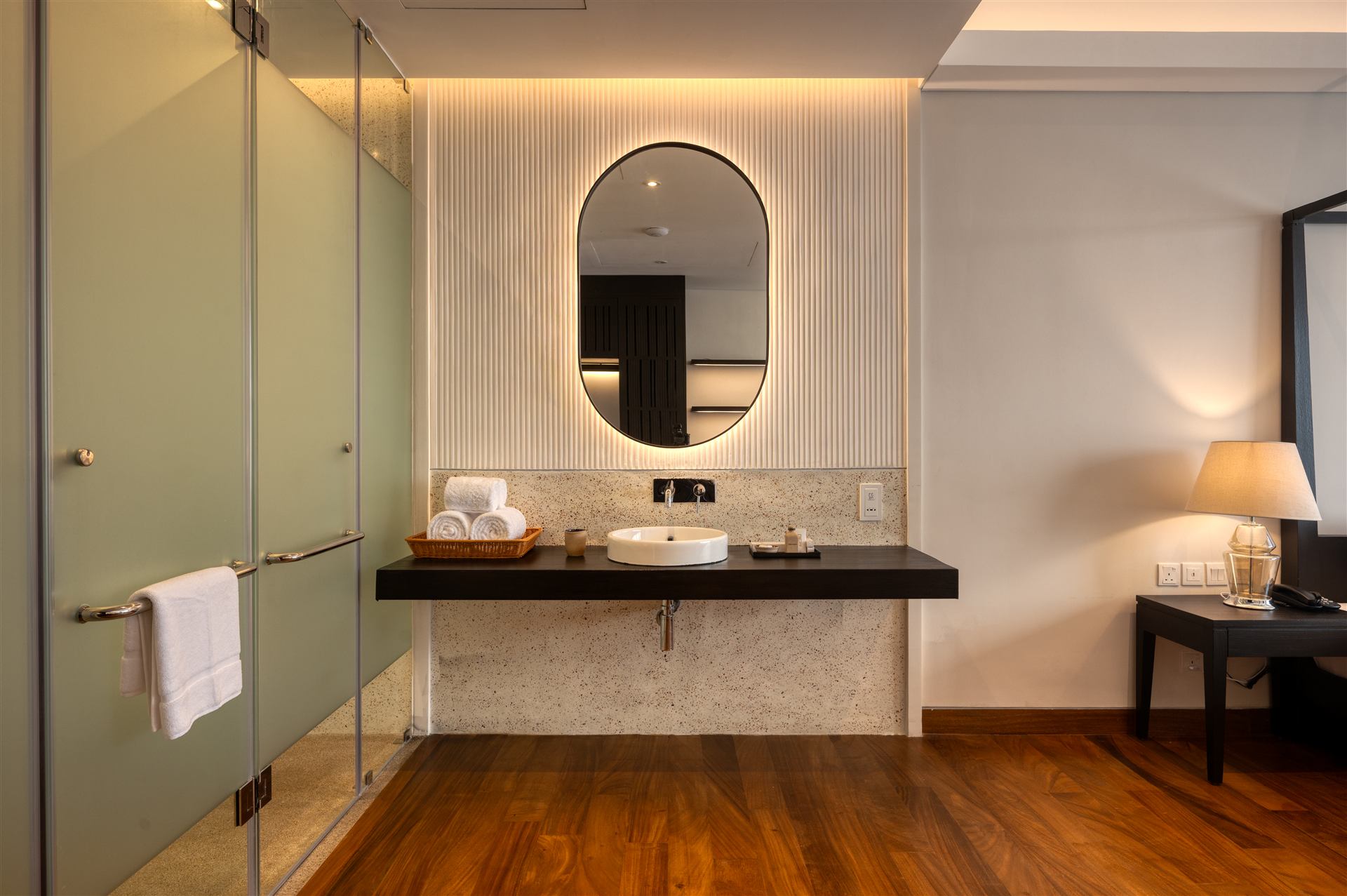 Room vanity with oval mirror and glass-walled shower