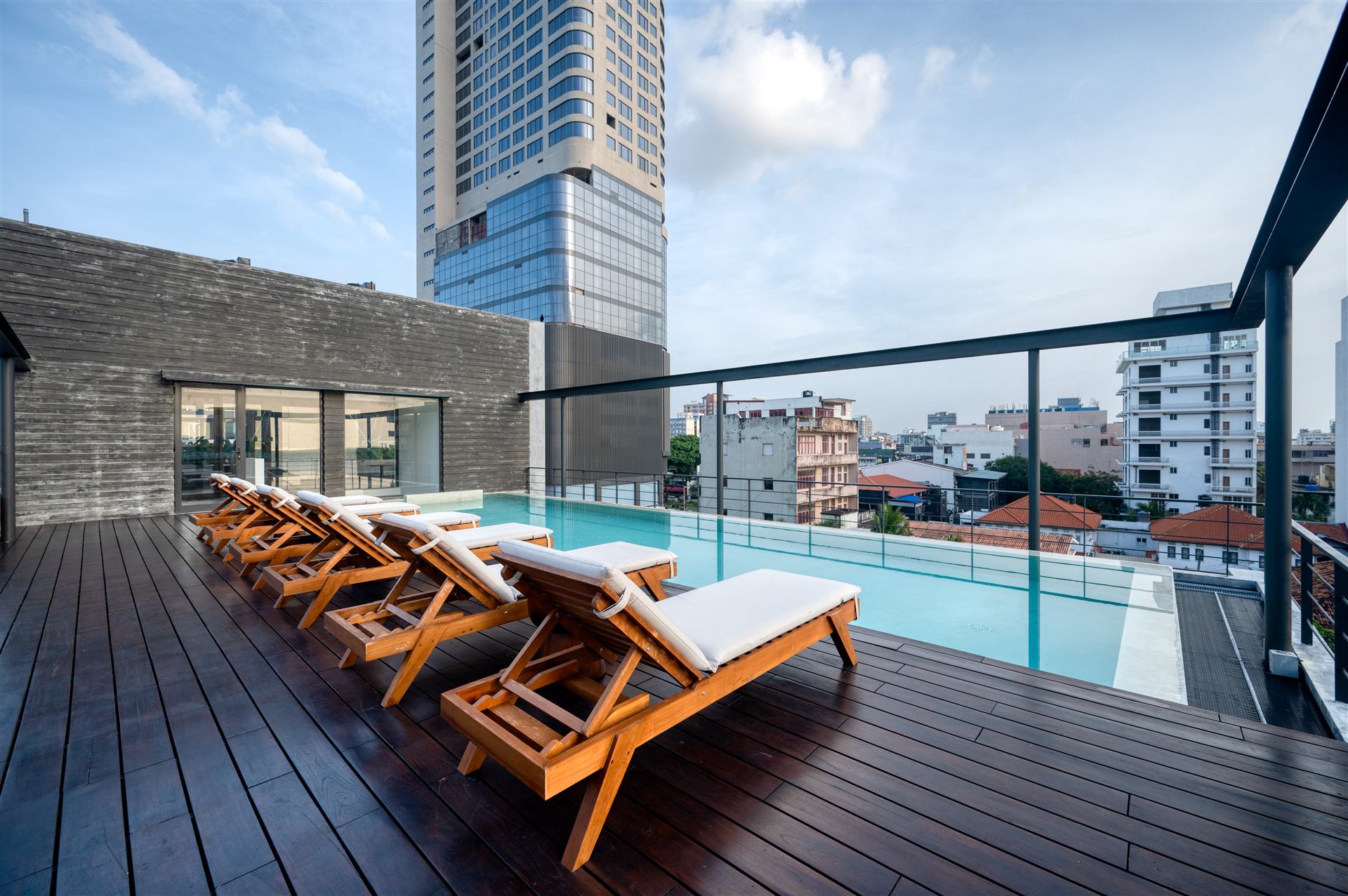 Rooftop pool with timber deck, loungers and Colombo skyline